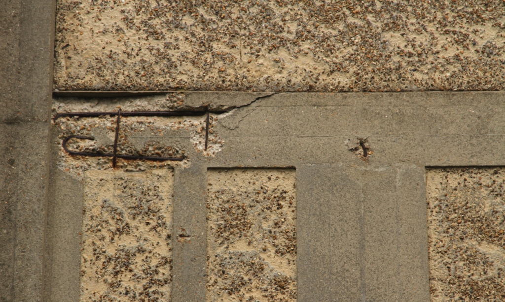 Close-up of concrete spalling damage showing exposed and rusting steel reinforcing bar (rebar) where concrete has broken away, demonstrating advanced freeze-thaw and corrosion damage