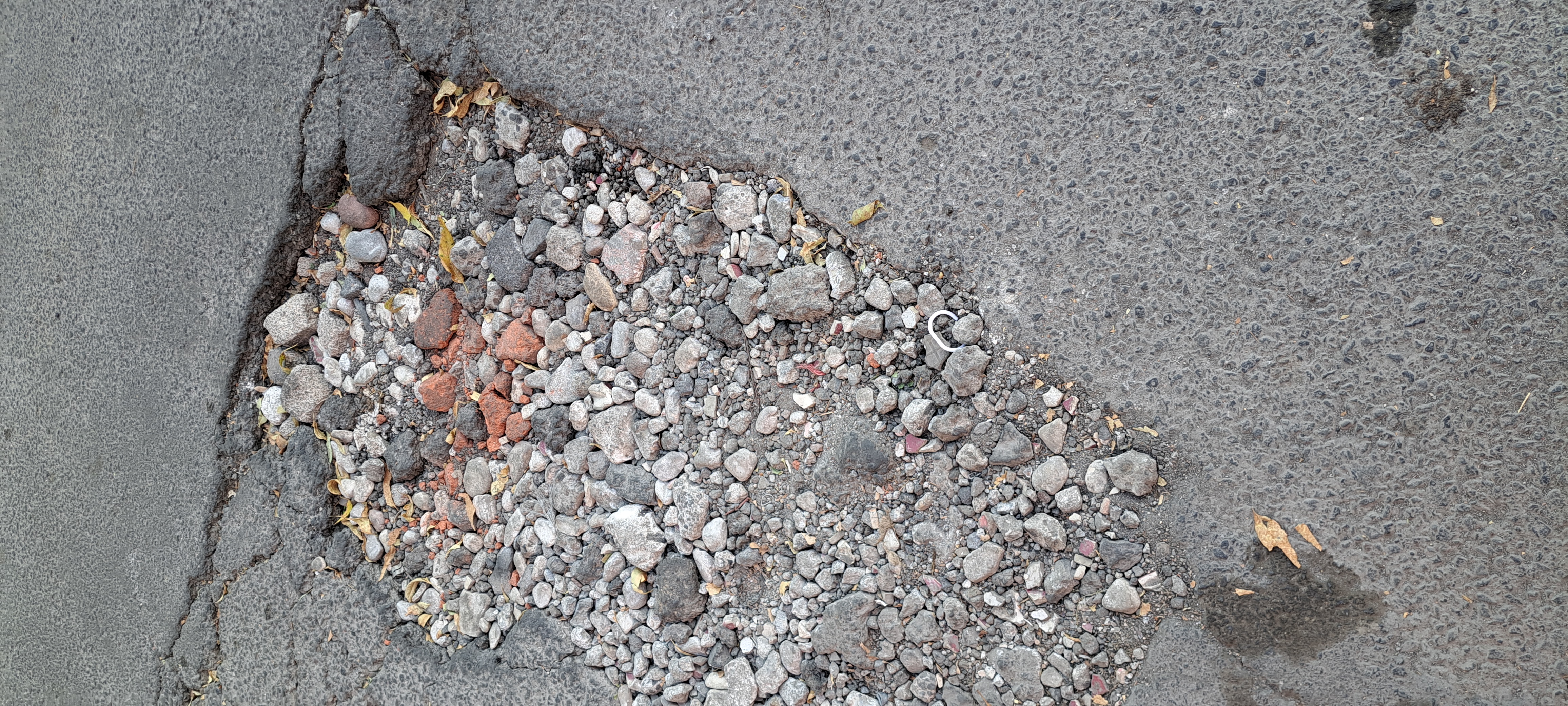 Severe concrete surface degradation showing the top layer broken away to reveal loose aggregate underneath, a common result of freeze-thaw cycling and de-icing salt damage